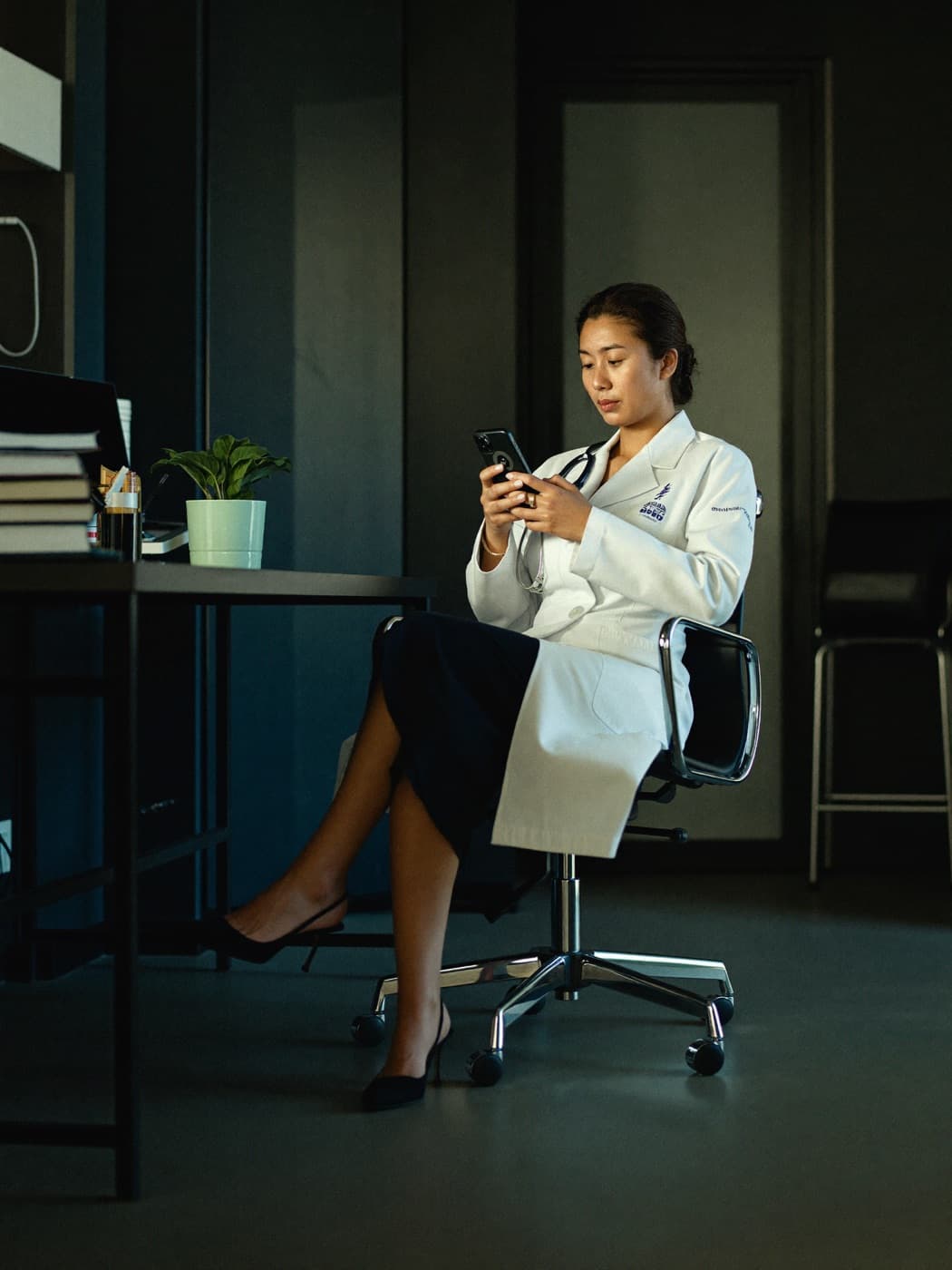 Médica lendo o celular no consultório entre uma consulta e outra