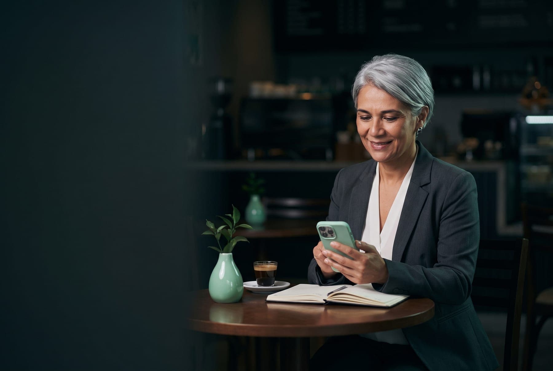 Consultora numa mesa de café com caderno aberto, lendo o celular antes de uma reunião